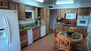 A kitchen with wooden cabinets, a refrigerator, a dishwasher, a sink, and a dining table with chairs. - Comfortable for travelers tired of staying at hotels. (Kingman)