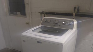 A Maytag washer and dryer unit in a laundry room with a white tiled wall and a door with a window. - Comfortable for travelers tired of staying at hotels. (Kingman)