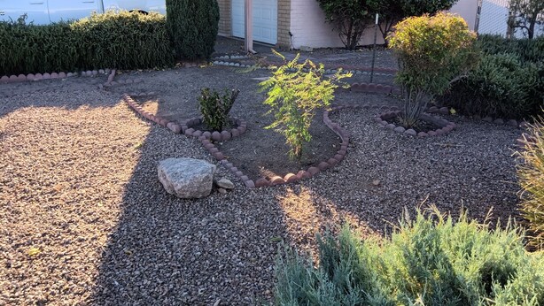A residential driveway with a gravel surface, a small garden with various plants, and a white pickup truck parked on the left. - Comfortable for travelers tired of staying at hotels. (Kingman)
