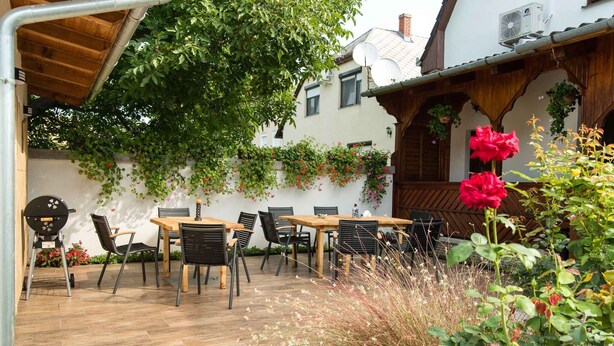 Une terrasse extérieure avec des tables et des chaises en bois, entourée d’une végétation luxuriante et de plantes en fleurs.