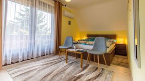 Une chambre à coucher avec un lit, deux chaises, un bureau, une lampe et une fenêtre avec des rideaux.