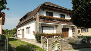 Une maison à deux étages, dotée d’un toit en pente, d’une entrée avec une allée fermée par un portail et d’un petit jardin agrémenté de plantes à fleurs.