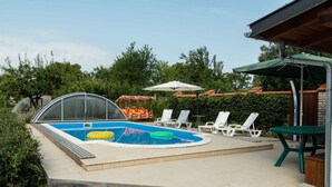 Une piscine dotée d’une zone partiellement abritée, entourée de chaises longues blanches et d’un espace salon couvert.