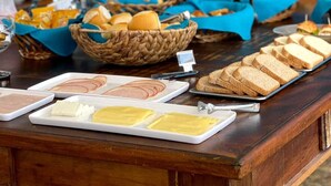 Disposição de buffet com diversos alimentos, incluindo pães e doces, e um espaço para café com várias máquinas.