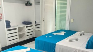 Quarto de hotel com duas camas, um guarda-roupa e uma janela com persianas.