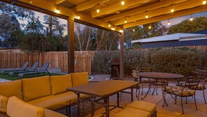 Una veranda esterna con un tavolo e sedie di legno, un divano in vimini e un barbecue.