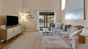Un soggiorno moderno con un'ampia TV a schermo piatto, un mobiletto in legno, un divano e vista su un giardino tramite una porta vetrata.