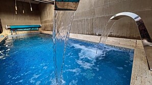 An indoor swimming pool with clear blue water, a bench, and a water feature. - Luxury Smart Loft in Bogota Chico , GYM POOL AND SPA  (Bogotá)