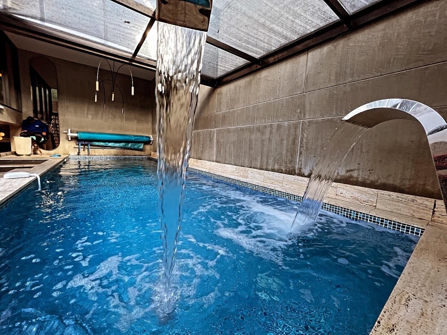 En inomhuspool med klart vatten, en hoppställning och en bänk.
