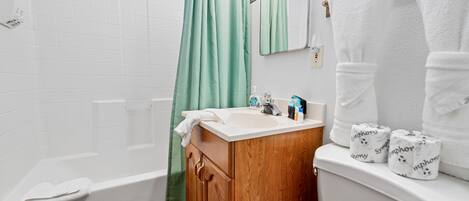 Ein Badezimmer mit einer Badewanne, einem hölzernen Waschtisch, einer Toilette und einem grünen Duschvorhang.