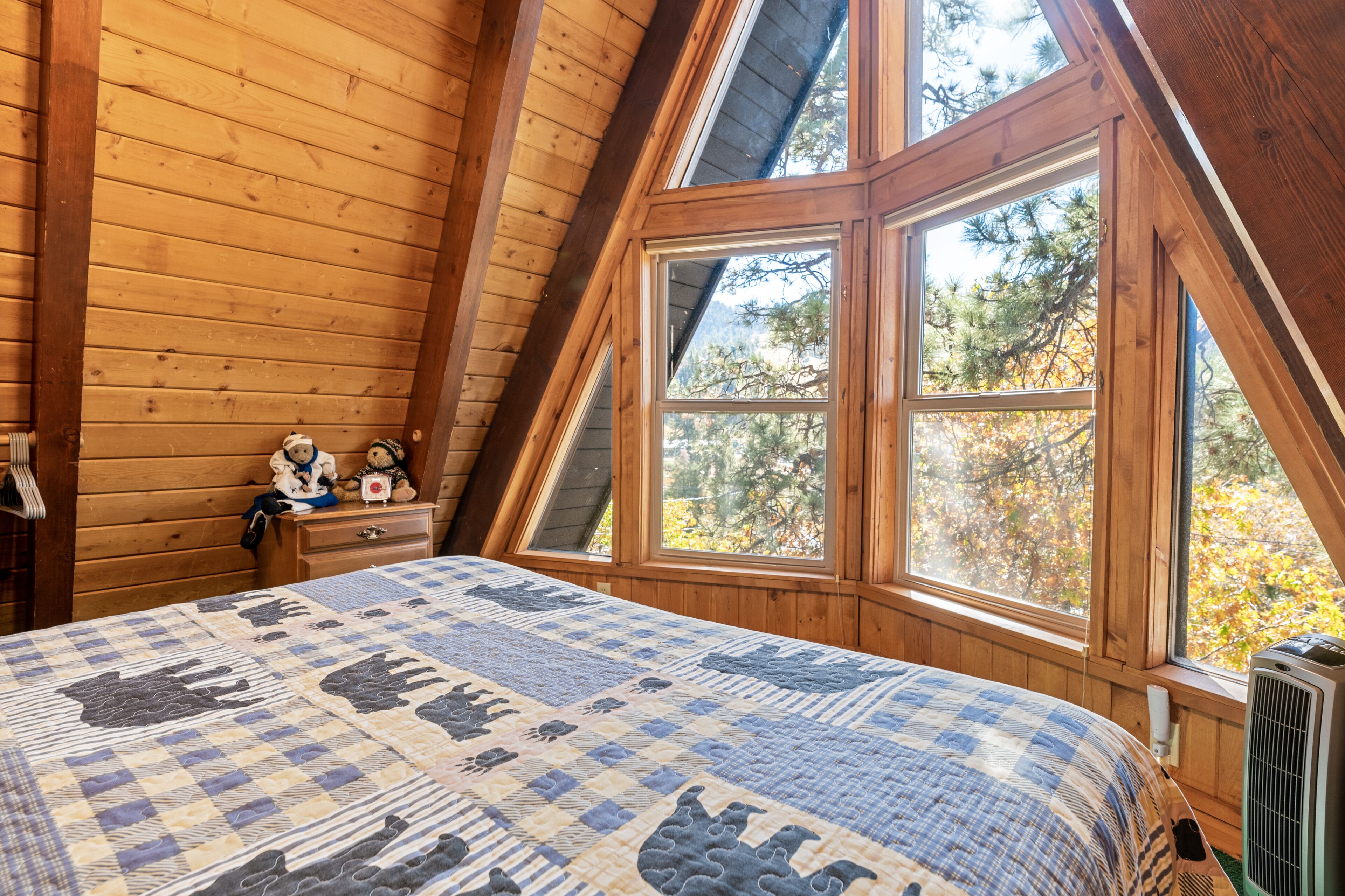 A bedroom with a sloped ceiling, a large window, a quilted bedspread, and a heater near the window.