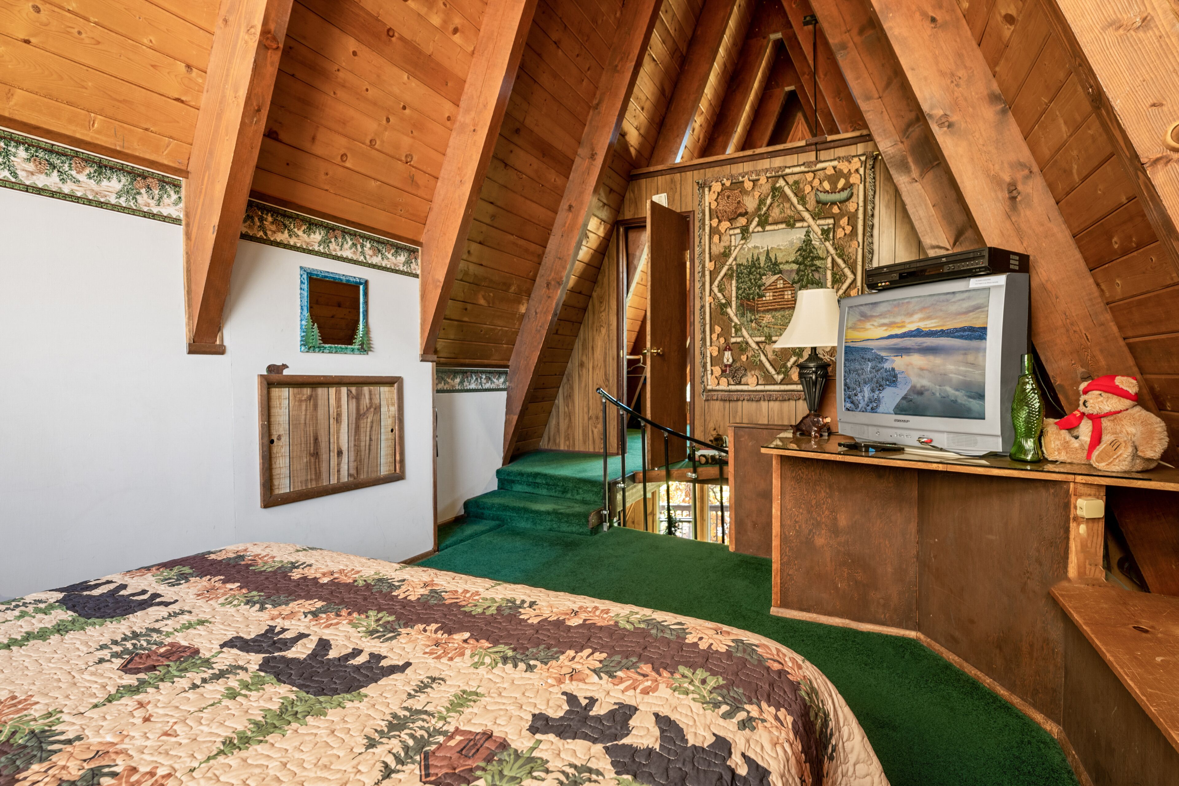 Une chambre confortable située dans les combles, avec un plafond en bois, un lit recouvert d’une courtepointe à motifs, une télévision et un ours en peluche.