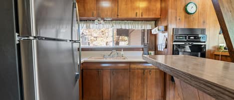 A kitchen with wooden cabinets, a stainless steel refrigerator, a sink, and a clock on the wall.