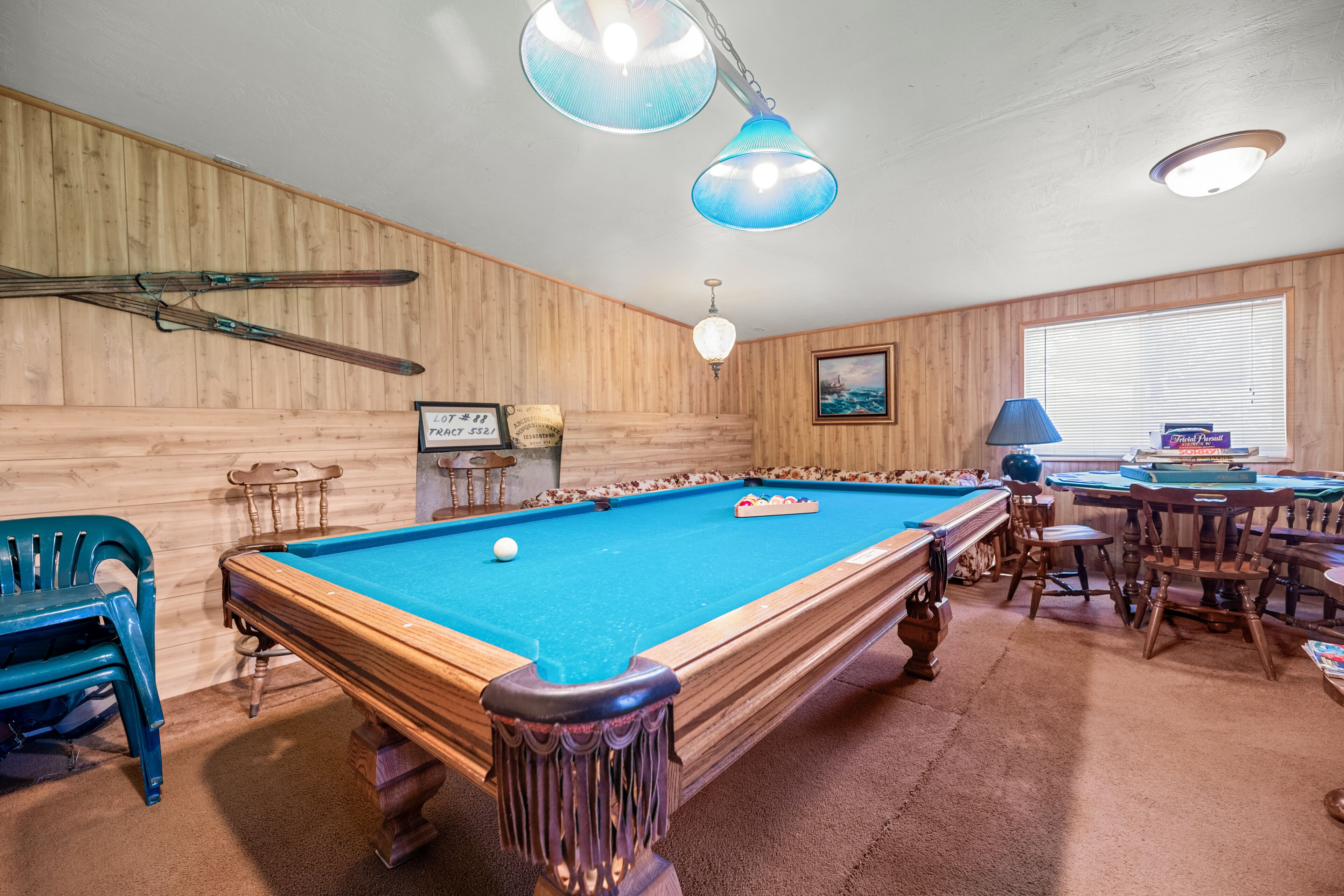 A pool table in a room with wooden walls, a blue ceiling light, and a window with blinds.