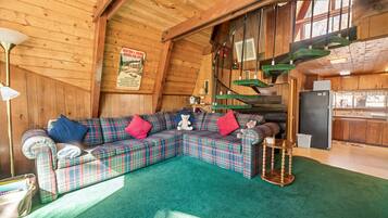 A cozy cabin interior with a plaid sofa, a small table, and a staircase.