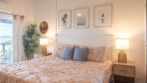 A bedroom with a large bed, two bedside lamps, a nightstand, a potted plant, and three framed pictures on the wall. - Flamingo House • ISLA • Sunset view • Walk to town (Cruz Bay)