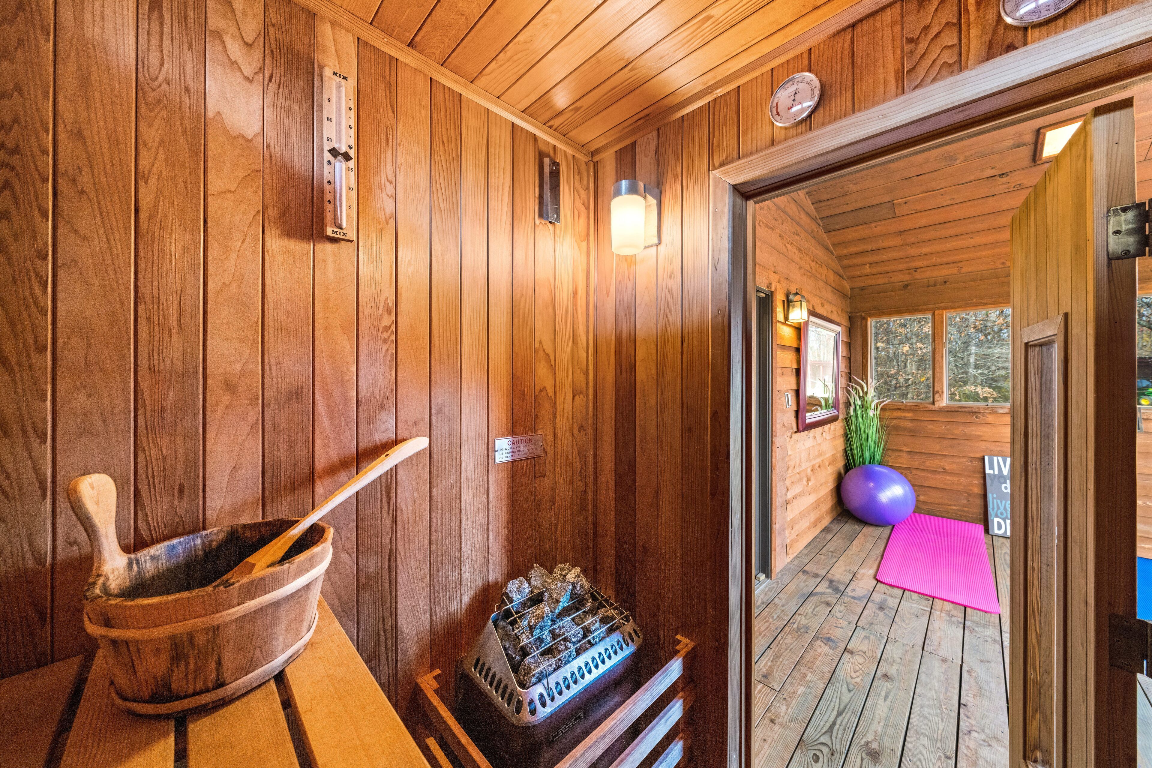 Una sauna de madera con un balde de madera, un calentador de sauna y un tapete rosa en el suelo.