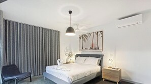A hotel room with a bed, a chair, a nightstand, a wall-mounted air conditioner, and a ceiling fan.