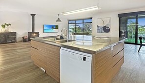 A modern kitchen with a dishwasher, wooden cabinets, a large island, and a view of the outdoors.
