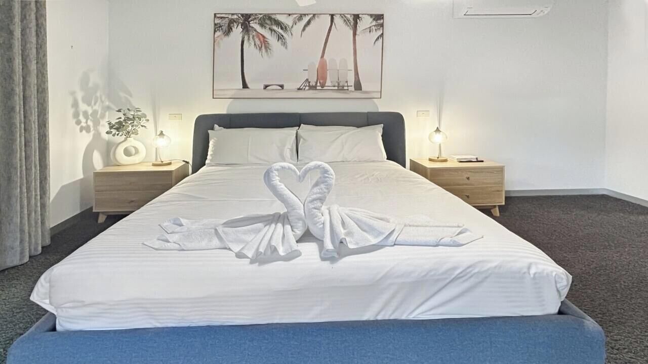 A hotel room with a bed, two bedside tables, a nightstand, a wall-mounted painting, and a window with curtains.