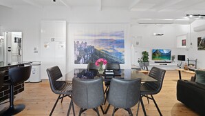 A modern living room with a glass dining table, black chairs, a large painting, a TV, and a sofa.
