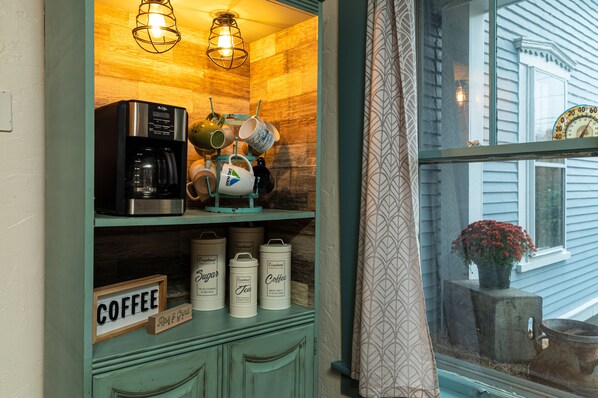Une cuisine équipée d’une machine à café, de tasses et de récipients étiquetés « Sucre » et « Café ».