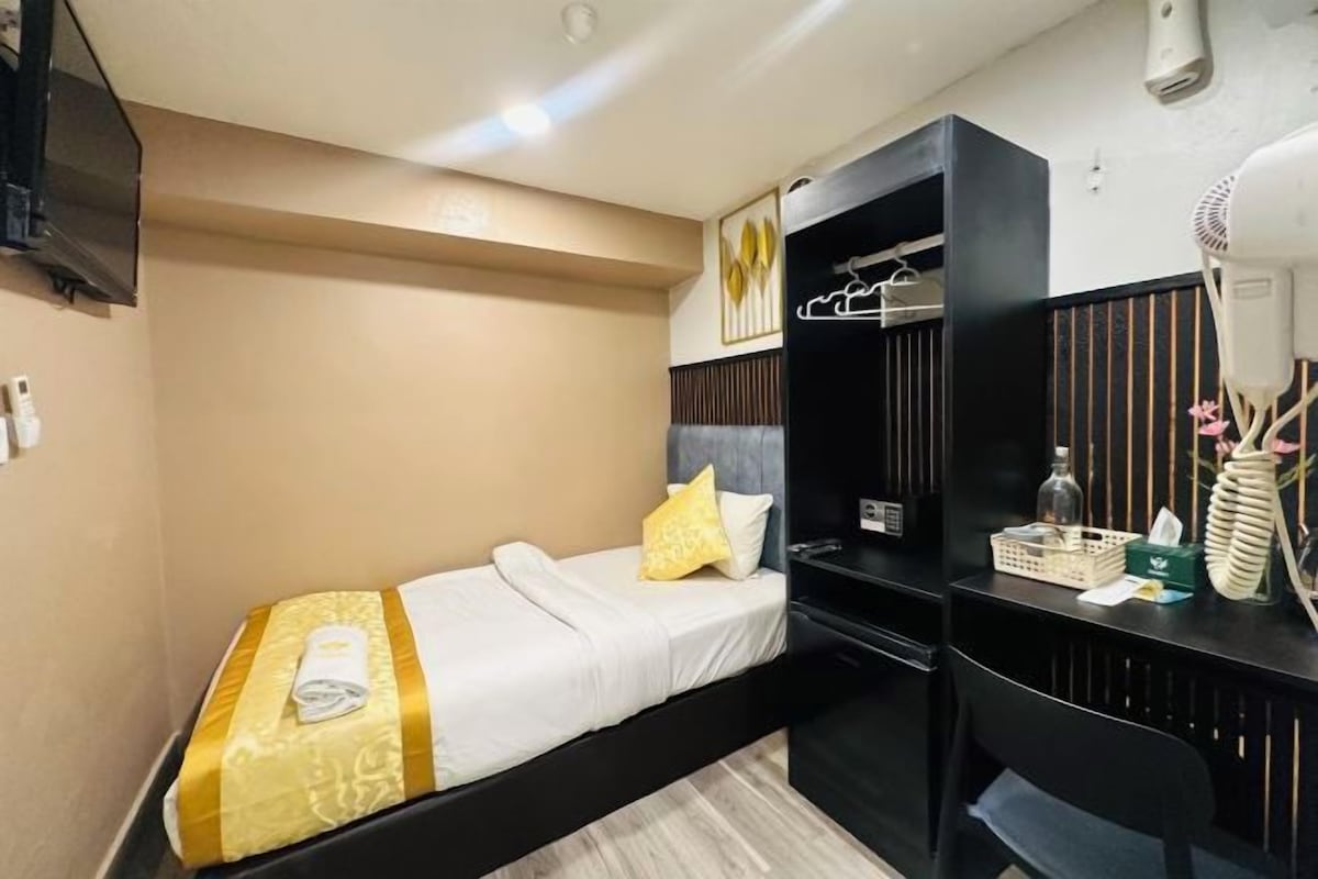 A single bed with a yellow bedspread, a desk with a chair, a mirror, and a TV mounted on the wall.