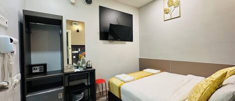 A hotel room with a bed, a desk with a mirror, a TV, a phone, and a clock on the wall.