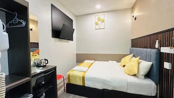 A hotel room with a bed, desk, chair, and a flat-screen TV.