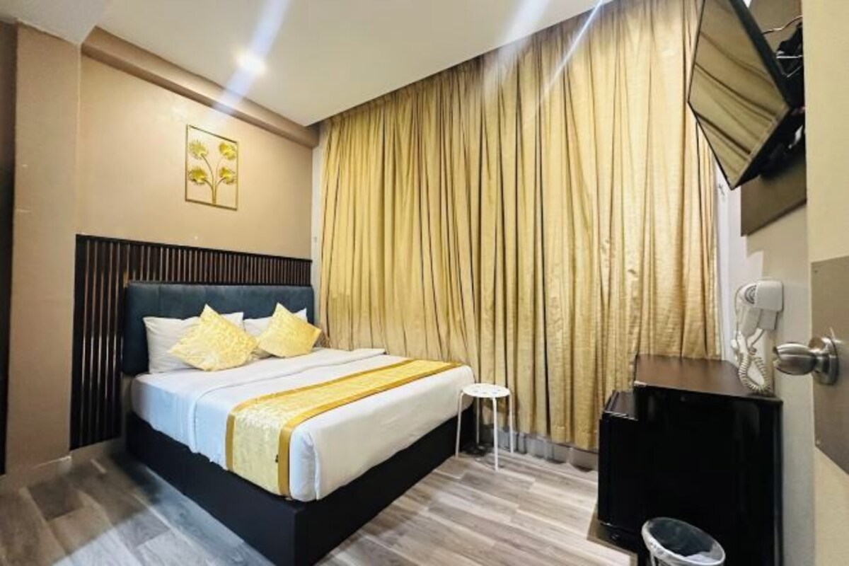 A hotel room with a bed, a bedside table, a mirror, and a curtain.