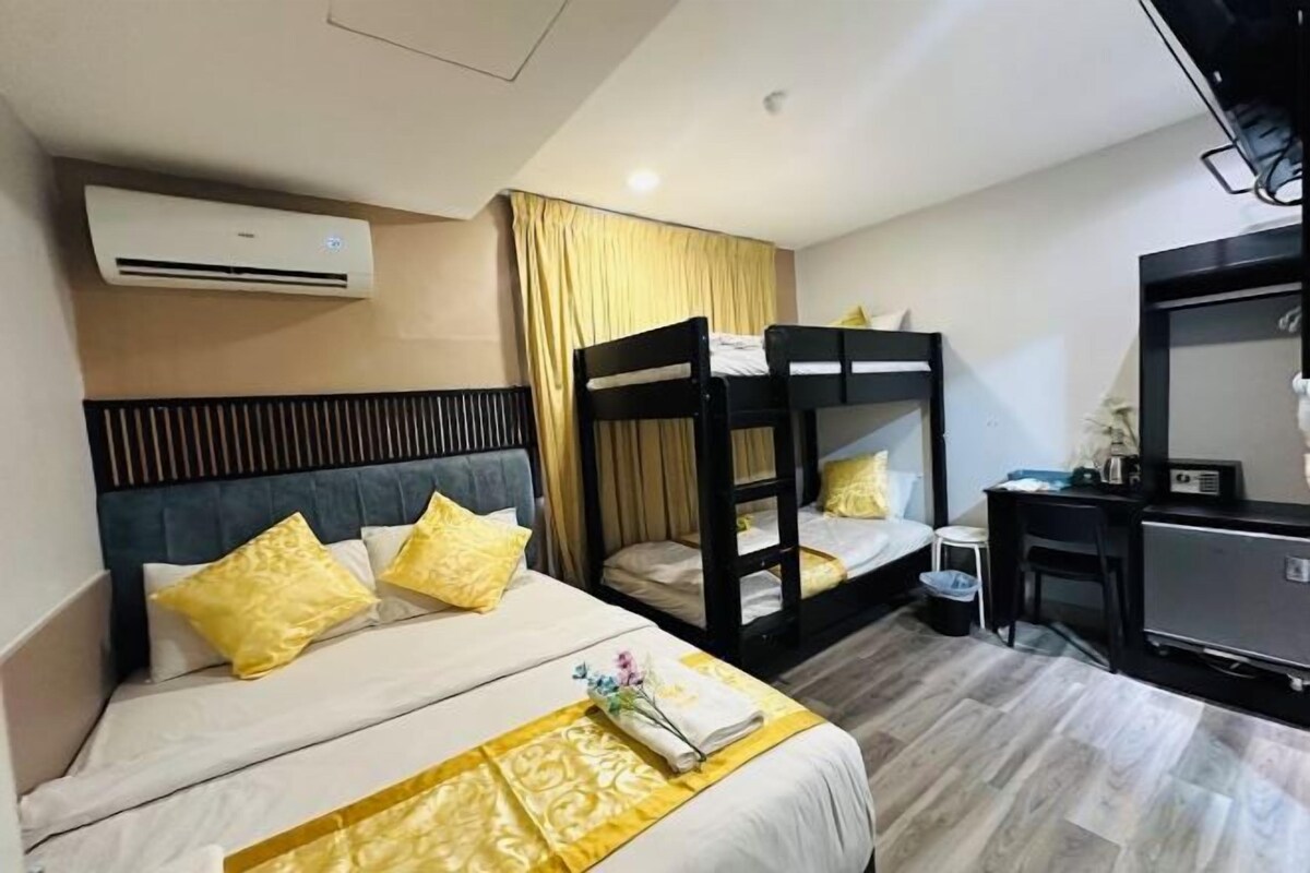 A hotel room with a bed, bunk beds, a desk, and a television.