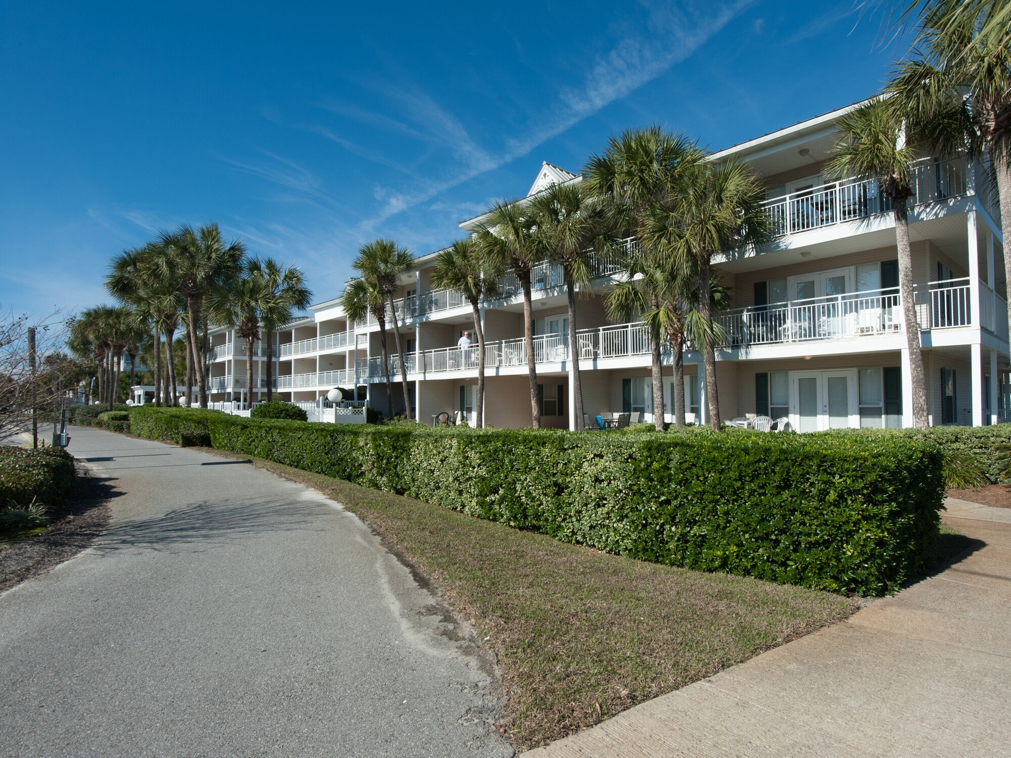 A multi-story hotel with balconies, palm trees, and a well-maintained lawn.
