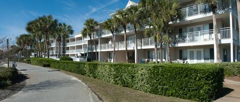 A multi-story hotel with balconies, palm trees, and a well-maintained lawn.