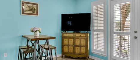 A room with teal walls, a wooden cabinet with a TV, two bar stools, and a framed picture on the wall.