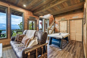 A wooden cabin interior with a sofa, a pool table, and a view of the mountains. - Hilltop retreat with breathtaking views. Close to all Gatlinburg has to offer!  (Gatlinburg)