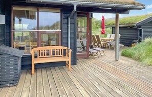 A wooden deck with a bench, a table with chairs, and a red umbrella.