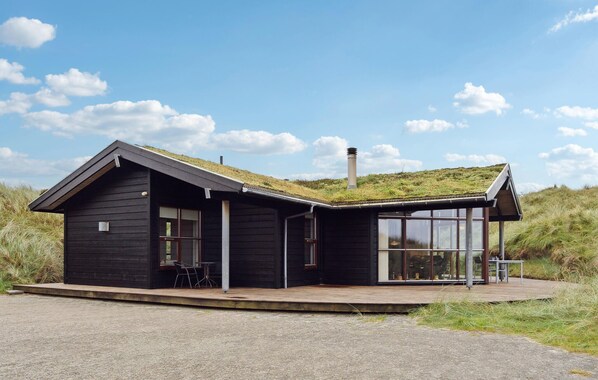 A modern black wooden cabin with a sloped roof, large windows, and a grassy hill in the background.