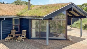 A modern house with a sloped roof, large glass windows, and a wooden deck with two chairs. - Beautiful home in Saltum (Saltum)