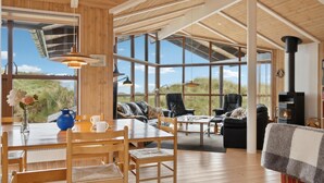 A spacious living area with a high ceiling, large windows, and a wood-burning stove. - Beautiful home in Saltum (Saltum)