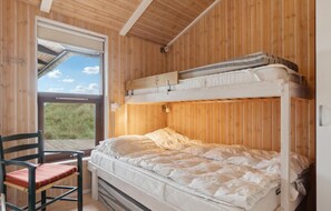 A bunk bed with a mattress and pillows, a chair with a cushion, and a window with a view of grass.