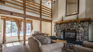 Una sala de estar acogedora con chimenea de piedra, techos altos y ventanas amplias con vistas a una piscina.