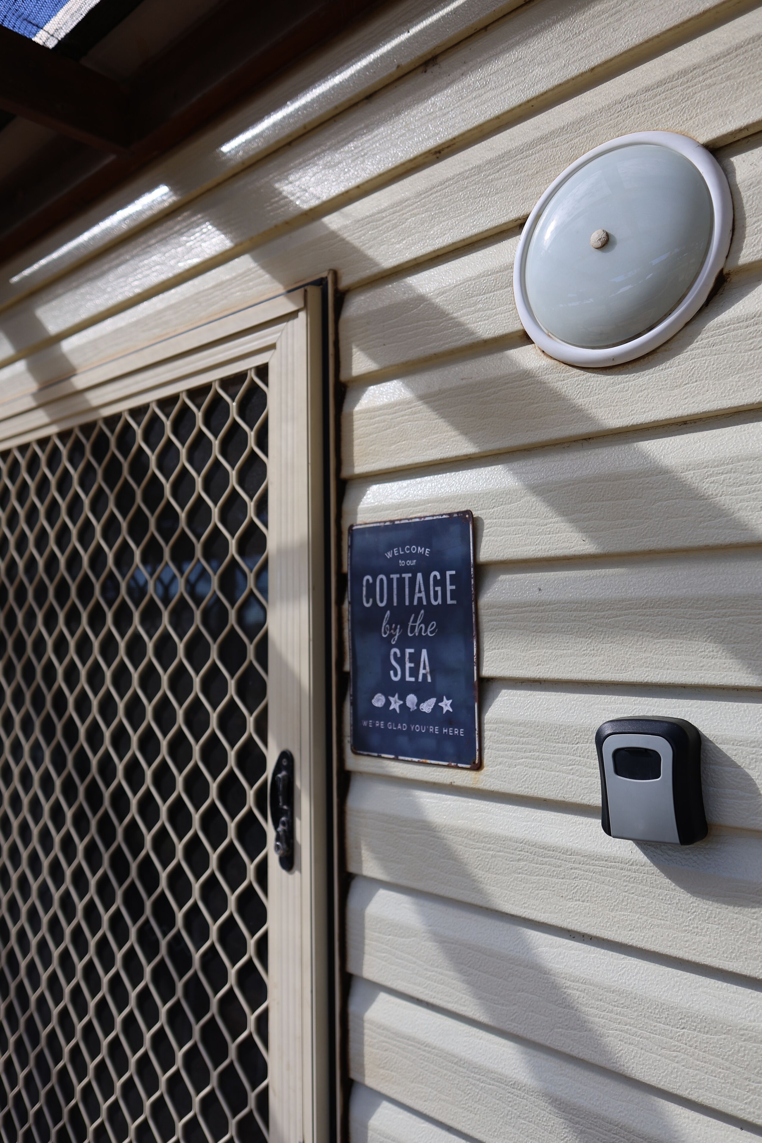 A cottage sign with the text "COTTAGE by the SEA" and a door with a mesh screen.