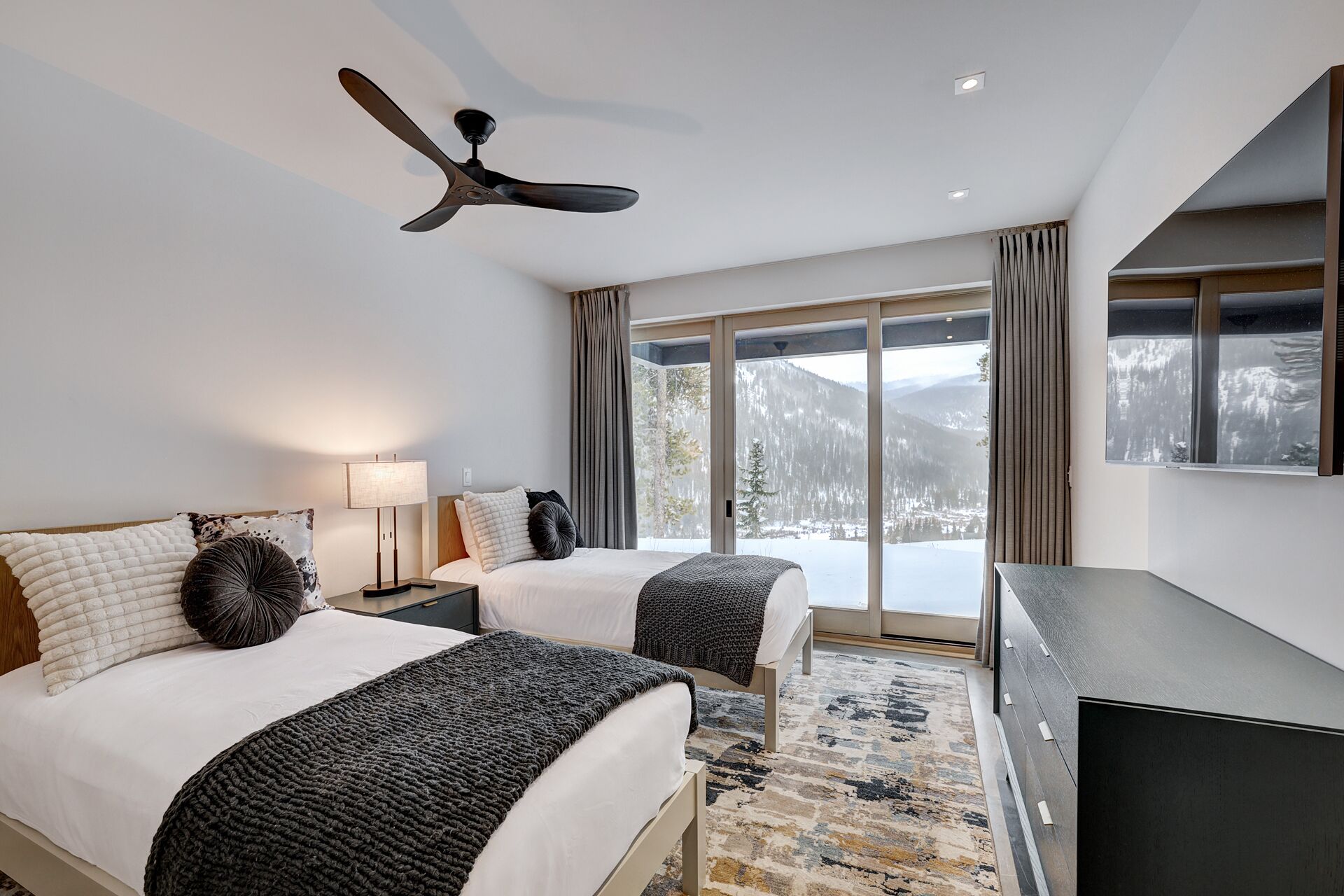 Une chambre d’hôtel avec deux lits, un ventilateur de plafond, une grande fenêtre donnant sur la montagne et un téléviseur à écran plat.