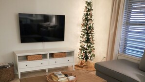 Een woonkamer met een grijze bank, een salontafel met boeken, een televisie aan de muur en een kerstboom.