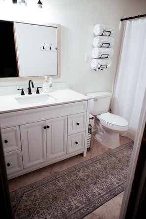 A bathroom with a white sink, black faucets, a white toilet, and a patterned rug on the floor.