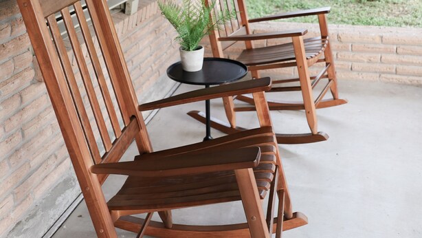 Twee houten schommelstoelen en een kleine tafel met een bloempot op een betonnen terras.
