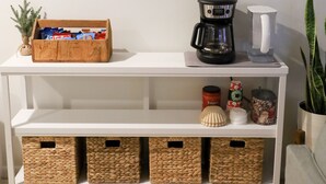 Een witte console tafel met een lijst rond een vogelillustratie, een koffiezetapparaat en rieten manden.