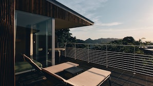 Een balkon met twee loungestoelen en een tafel, met uitzicht op een schilderachtig landschap met bergen en bomen.