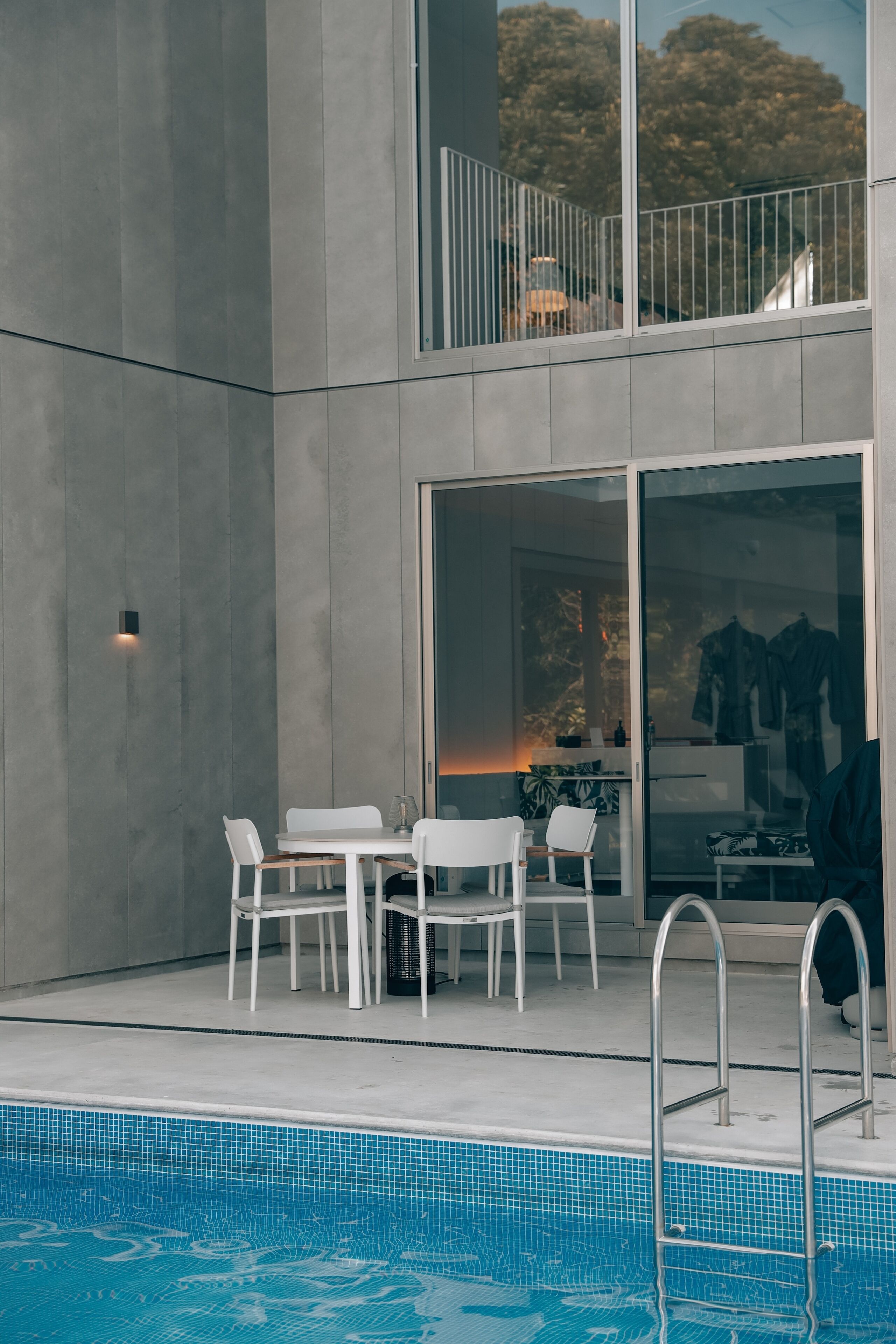 A modern outdoor pool area with a dining set and a glass door leading to a balcony.