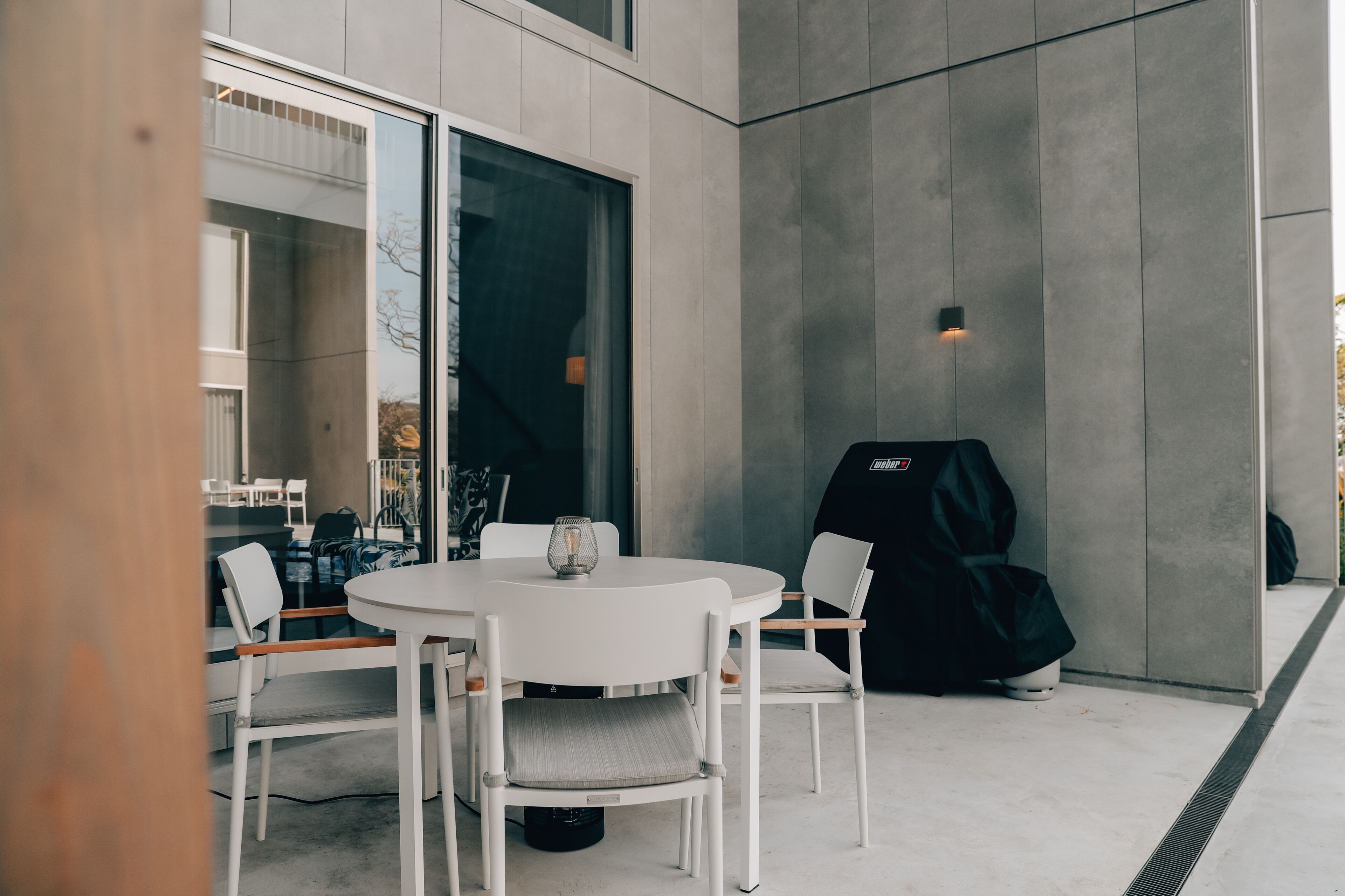 Un espace de restauration extérieur moderne, doté d’une table ronde et de quatre chaises, d’une cloison en verre et d’un chauffage d’extérieur noir.